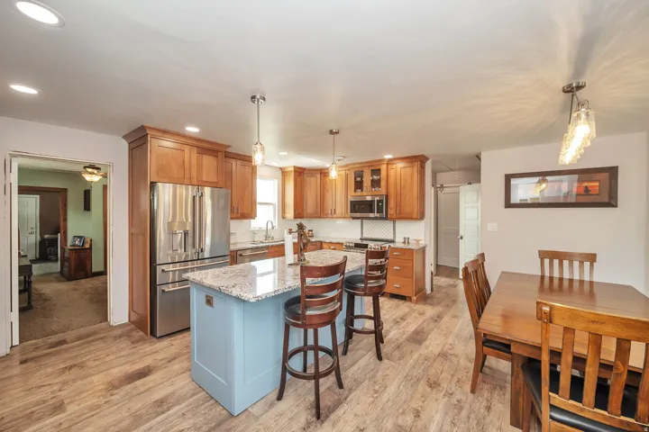 Kitchen featuring wood-finish flooring, a light blue island with a light-toned stone countertop, stainless steel appliances, and wood cabinetry