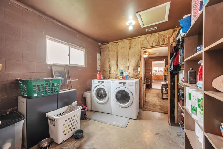 Dedicated laundry area featuring dual-pane windows, a concrete floor, built-in shelving, and exposed wall insulation