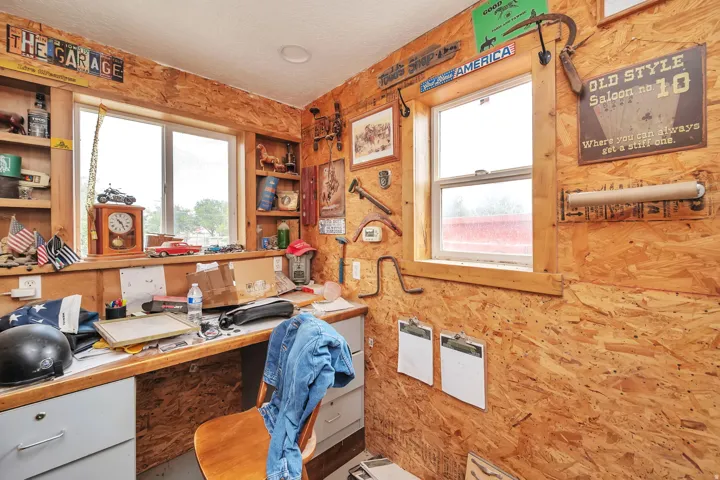 Workroom featuring oriented strand board walls, two windows with wood trim, and a built-in desk with under-counter cabinetry