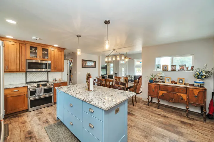Kitchen featuring a vibrant blue island with a stone-finish countertop, wood-finish flooring, recessed lighting, and stainless steel appliances