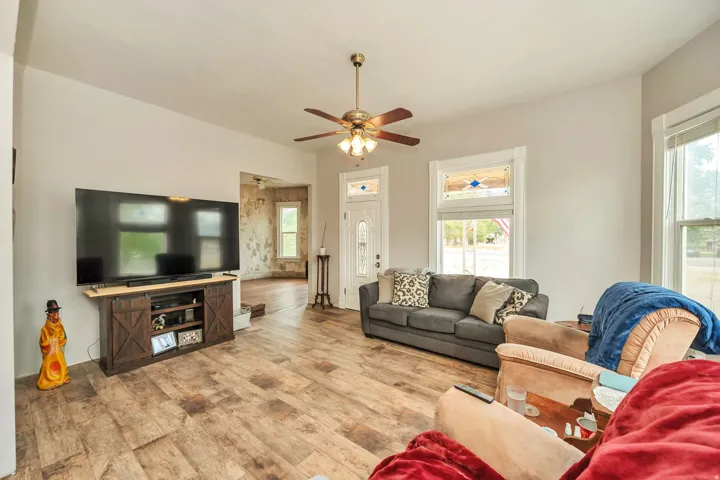 Spacious living area featuring wood-finish flooring, a ceiling fan with integrated lighting, and multiple windows with white trim