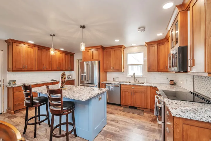 Kitchen featuring wood-finish cabinetry, stainless steel appliances, speckled countertops, and a subway tile backsplash