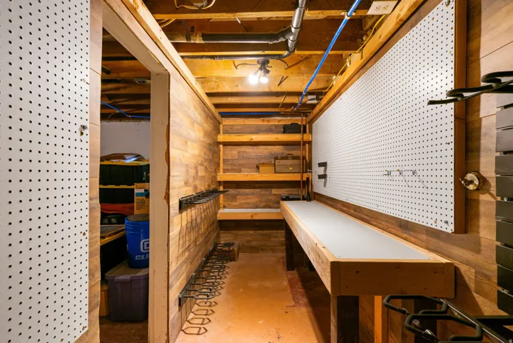 hidden work room with wood-finish wall paneling, exposed ceiling joists, and a built-in workbench featuring a light-colored surface