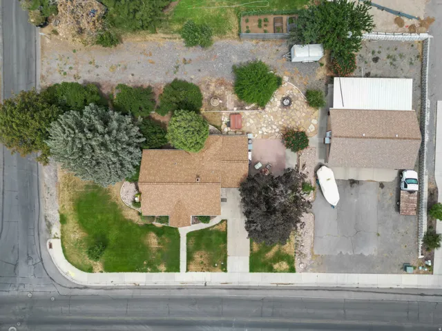 Corner lot property featuring a main residence with a prominent shingle roof, an expansive paved driveway, and established landscaping