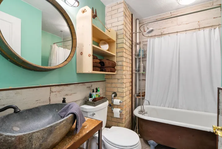Bathroom featuring a freestanding tub with a shower fixture, a stone vessel sink, and a circular wood-framed mirror