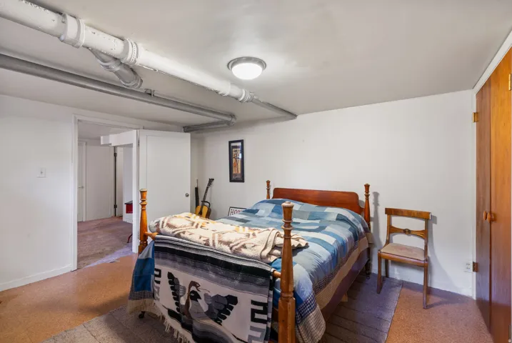 Room featuring white walls, a flush-mount ceiling light, and exposed ceiling pipes
