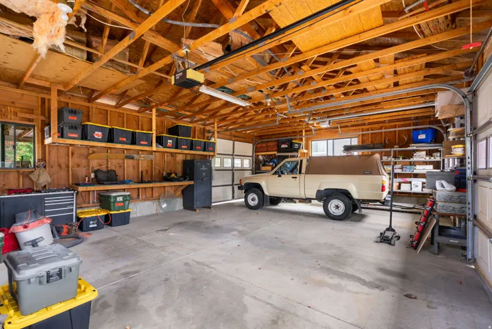 Spacious garage featuring concrete flooring, exposed wood beam ceiling, two overhead garage doors, built-in shelving, and a workbench area