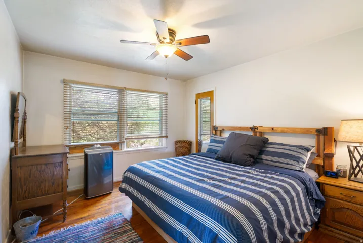 Bedroom featuring wood-finish flooring, a ceiling fan with light fixture, and a window with blinds
