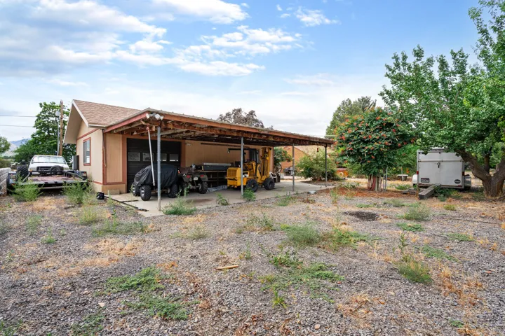 Detached garage with a covered carport extension, featuring a light brown exterior and a shingle roof