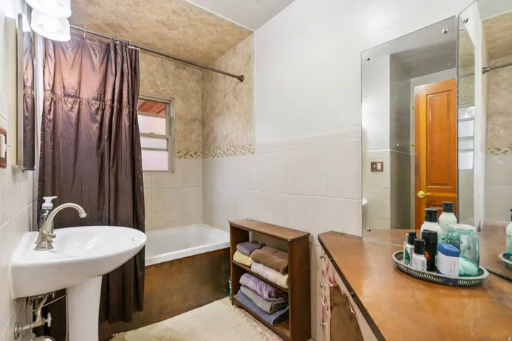 Full bathroom featuring a pedestal sink, white bathtub with a window, and varied tilework