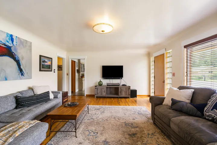 Living area featuring wood-finish flooring, a flush-mount ceiling light, and a window with horizontal blinds
