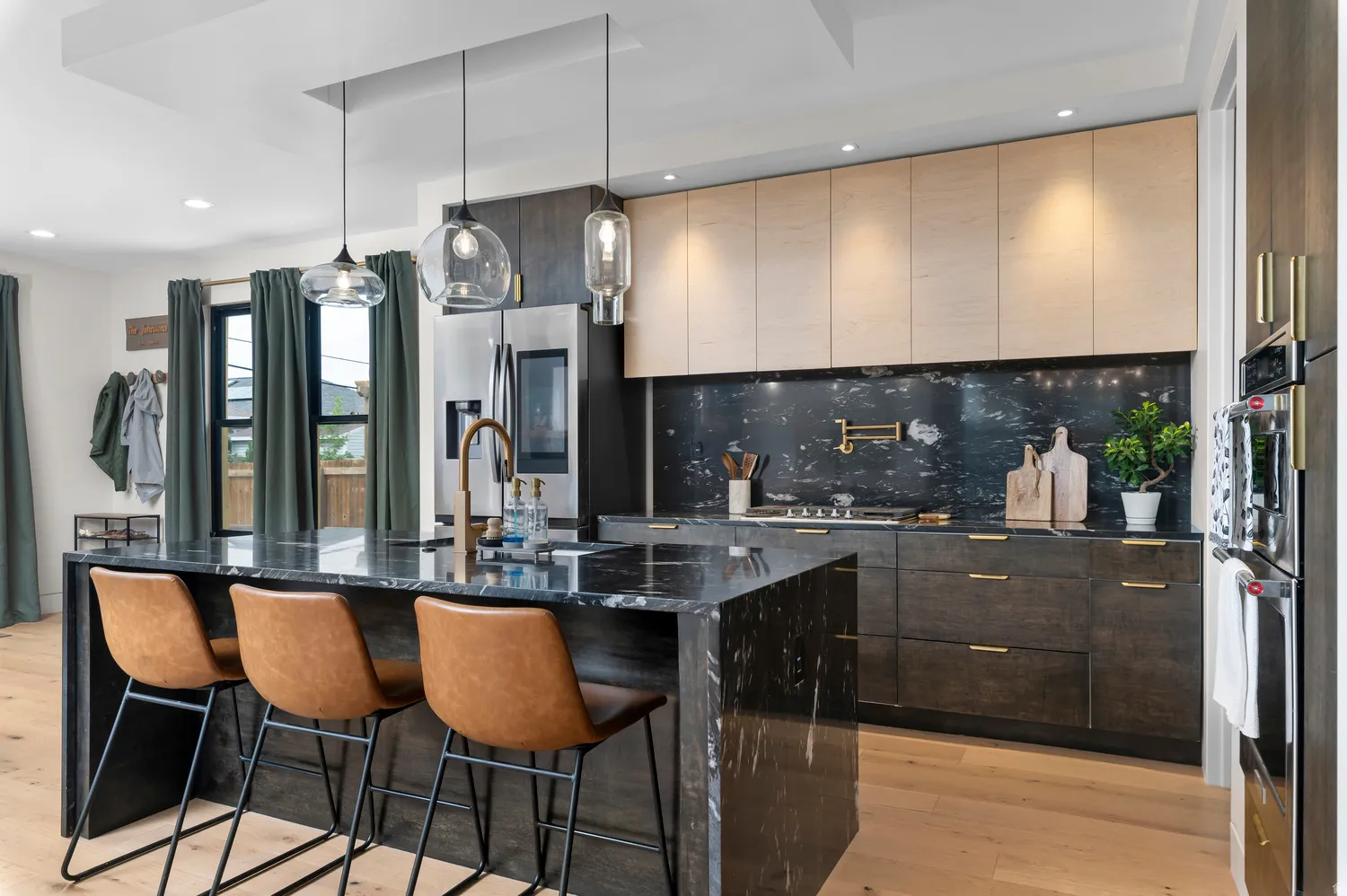 Gourmet kitchen featuring a large waterfall island with seating, dark stone countertops and backsplash, integrated stainless steel appliances, and two-tone cabinetry with gold-tone hardware