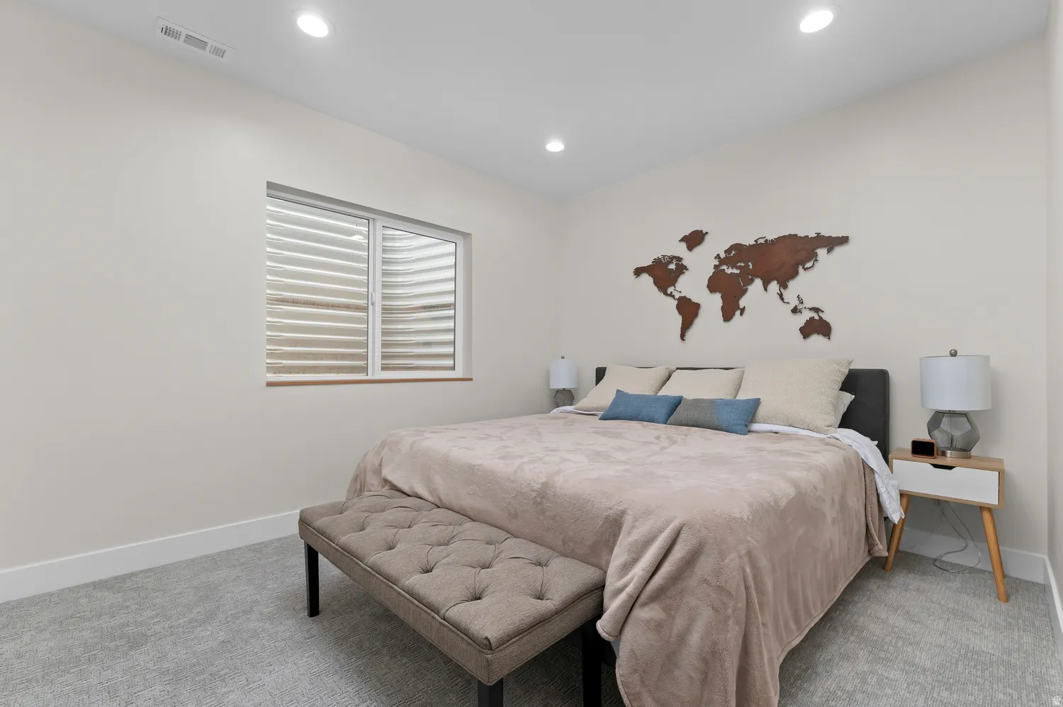 Bright bedroom space featuring a window with integrated blinds, recessed ceiling lighting, textured wall decor, and light-toned carpeting