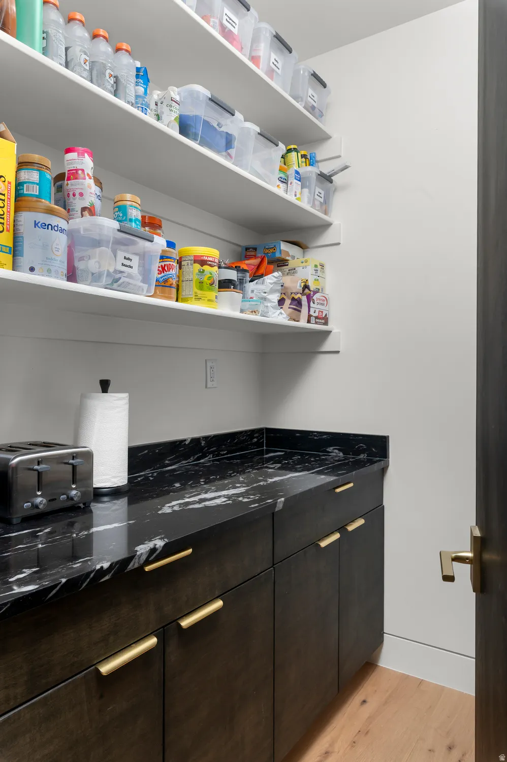 Dark wood-finish cabinetry with gold-tone hardware, a black marbled countertop, and light wood-finish flooring