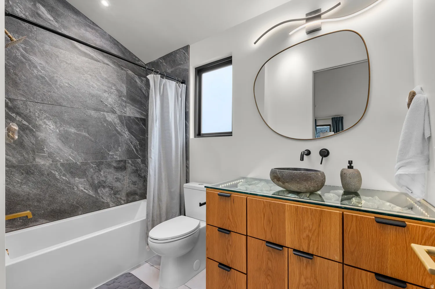 Contemporary bathroom featuring a unique stone vessel sink, wall-mounted matte black faucet, and a custom wood-finish vanity with a glass countertop