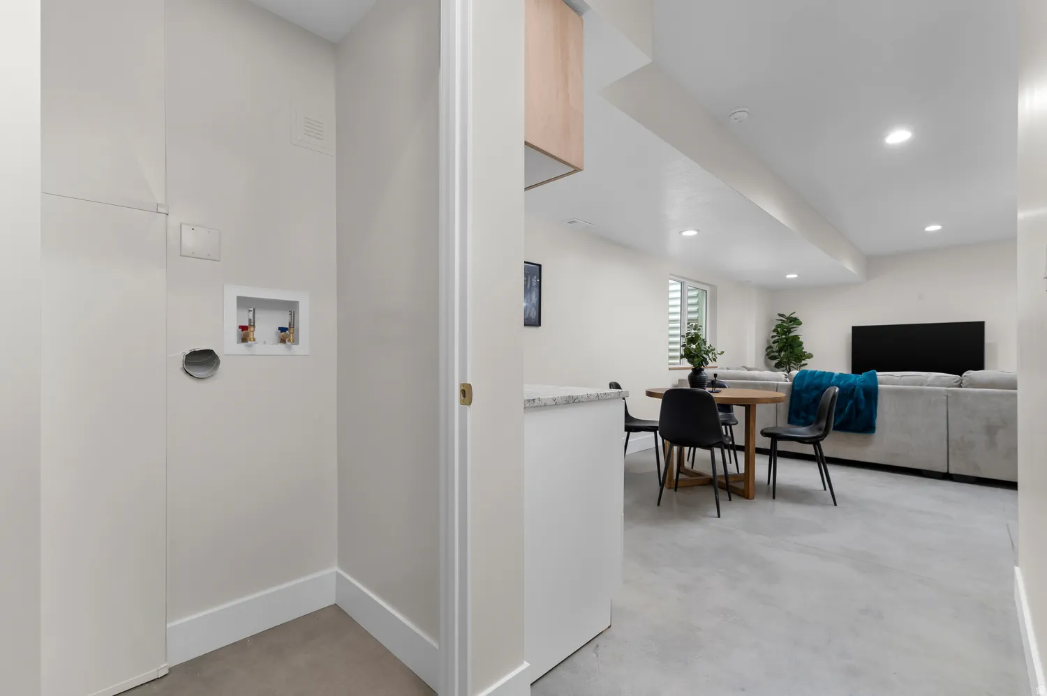 Dedicated laundry area featuring water hookups and a dryer vent, complementing the open entertainment space with recessed lighting and light-toned flooring