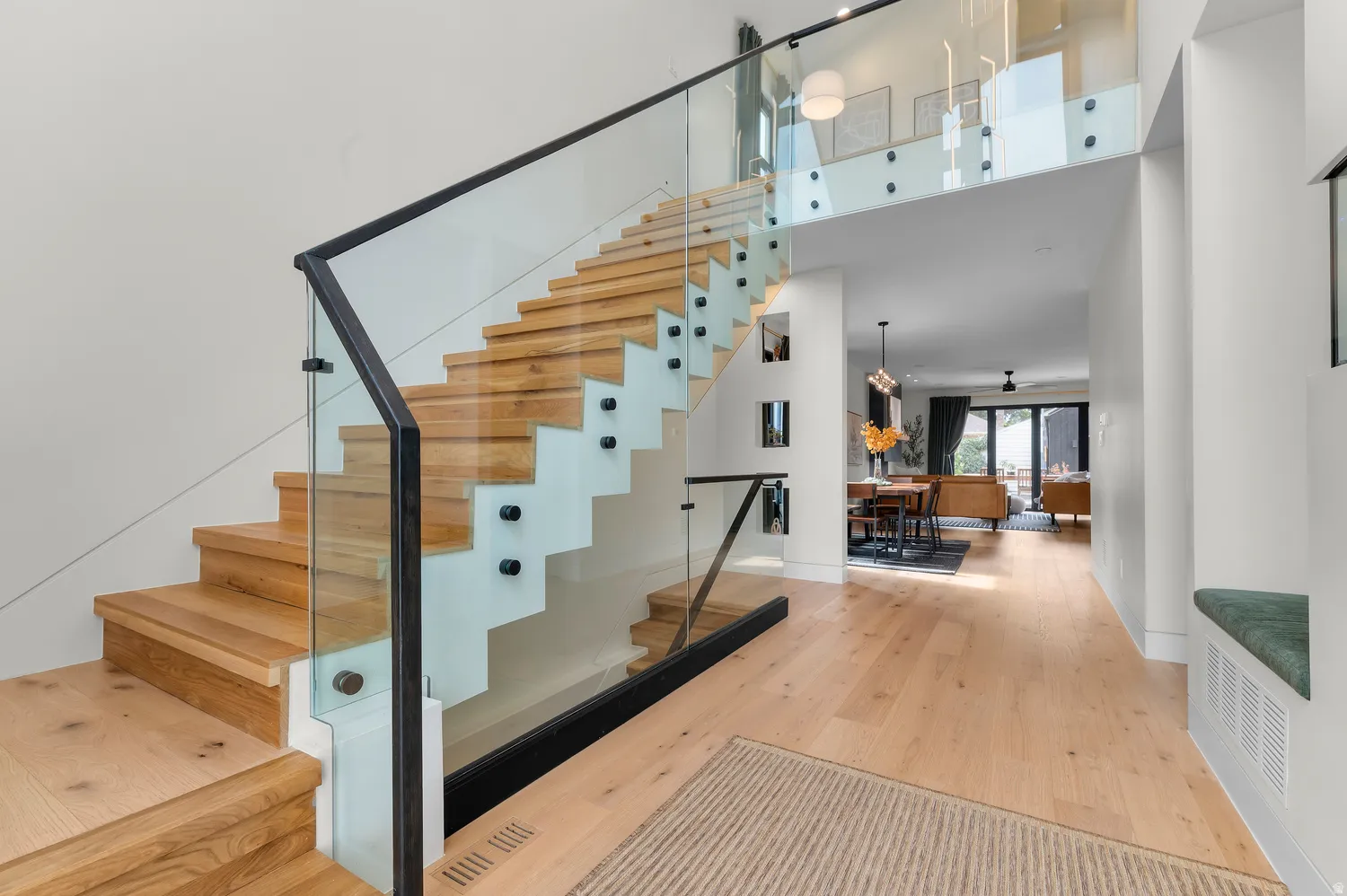 Modern interior featuring light wood-finish flooring, a contemporary staircase with glass railings and dark banisters, and a built-in bench seat