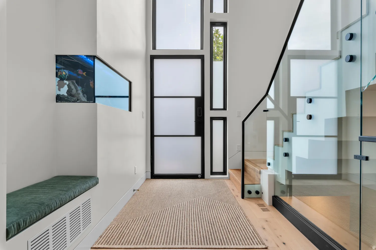 Modern entryway featuring a multi-paneled frosted glass door and surrounding windows, light wood-finish flooring, and a contemporary staircase with glass railing