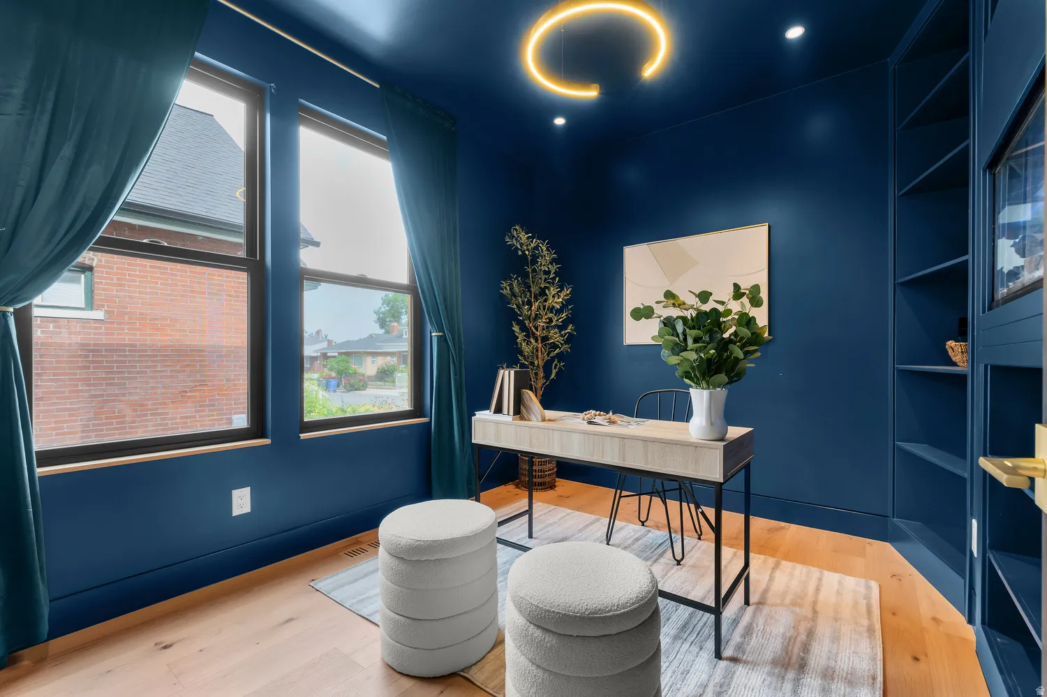 Dedicated room featuring rich blue walls, hardwood-finish flooring, built-in shelving, ample natural light from multiple windows, and recessed lighting