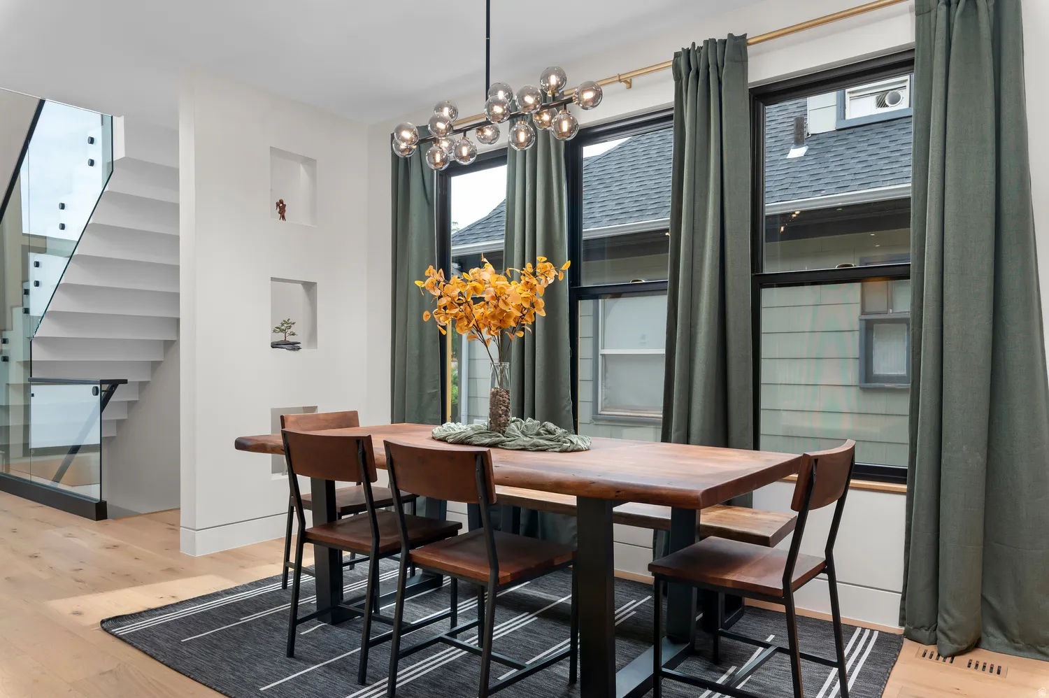 Modern dining area featuring a linear chandelier, light wood-finish flooring, and recessed wall niches