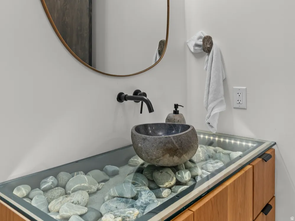 Custom vanity with a glass-covered river rock display, featuring a dark stone vessel sink and a matte black wall-mounted faucet