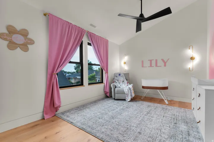 Vaulted ceiling with a black ceiling fan, dual wall sconces, wood-finish flooring, and two windowpanes