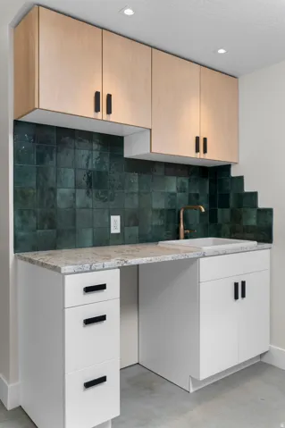 Custom cabinetry featuring light wood-finish uppers and white base units, complemented by a mottled green tile backsplash
