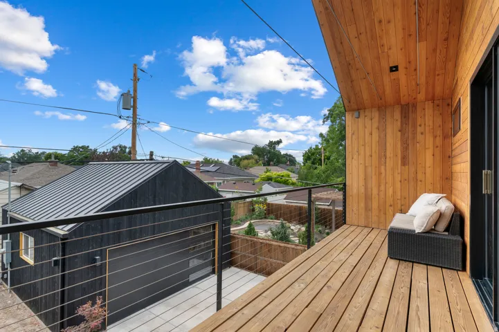 Wood-finish balcony with black metal railing and cable infill, featuring an exterior wood-paneled wall and ceiling