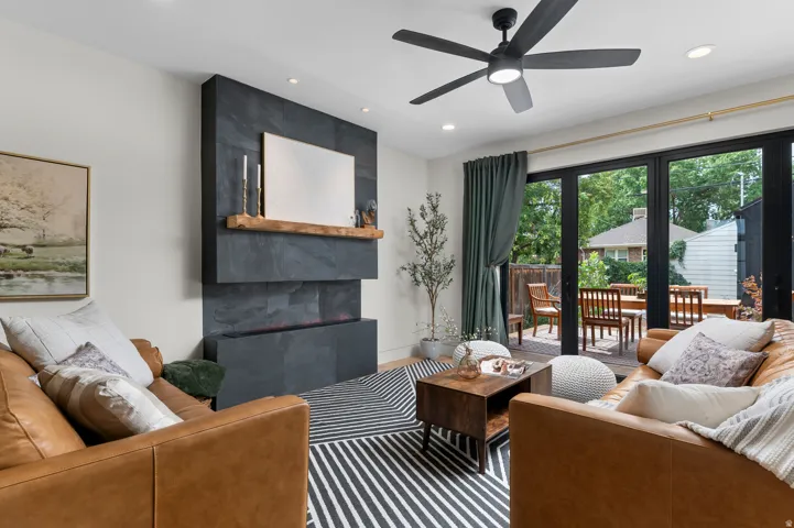 Living space featuring a slate-clad electric fireplace with a wood mantle, a ceiling fan, recessed lighting, and large folding patio doors opening to an outdoor deck