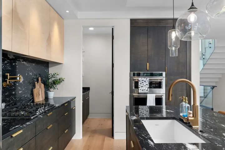 Gourmet kitchen showcasing black stone countertops and backsplash, integrated stainless steel double ovens, and a gas cooktop with a pot filler