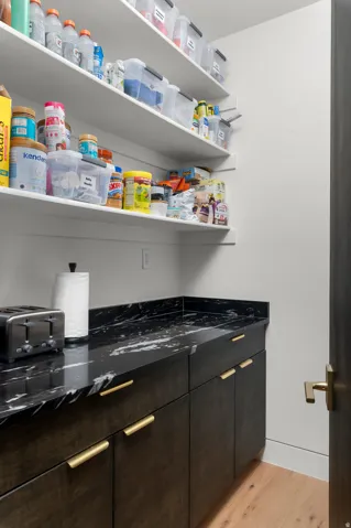 Dark wood-finish cabinetry with gold-tone hardware, a black marbled countertop, and light wood-finish flooring