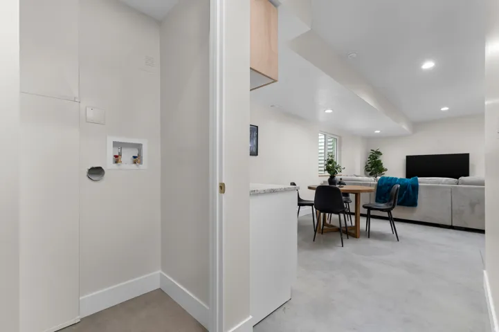 Dedicated laundry area featuring water hookups and a dryer vent, complementing the open entertainment space with recessed lighting and light-toned flooring