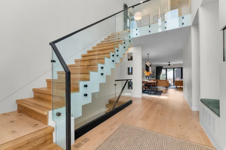 Modern interior featuring light wood-finish flooring, a contemporary staircase with glass railings and dark banisters, and a built-in bench seat