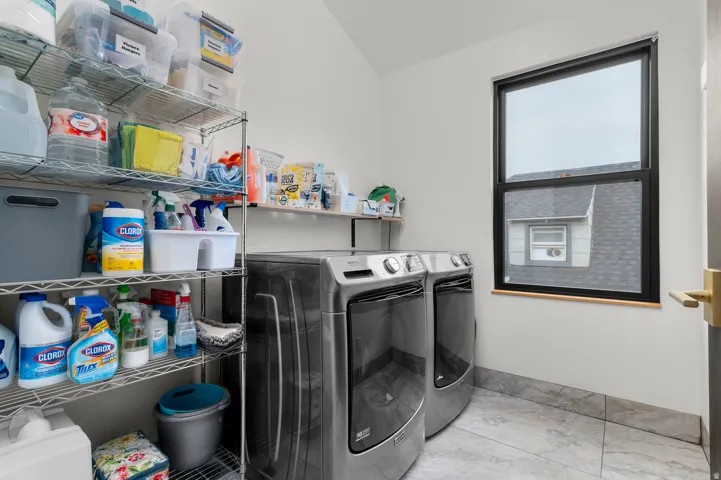 Dedicated laundry area featuring a large window, tiled flooring, light-colored walls, and a substantial wire shelving system