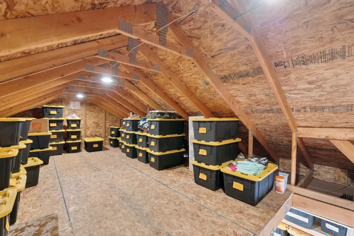 Storage above garage. Spacious attic storage area featuring exposed wood beams and oriented strand board walls