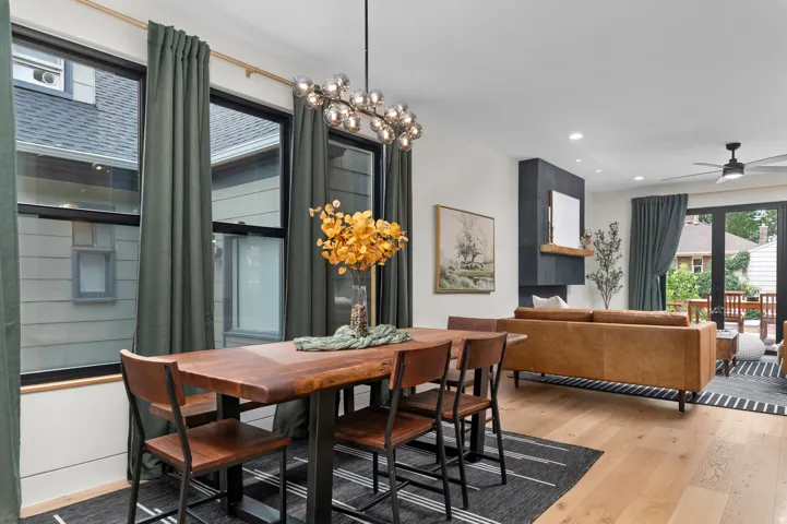 Open-concept living area featuring light wood-finish flooring, a contemporary fireplace with dark tile surround and wood mantel, recessed lighting, and a ceiling fan