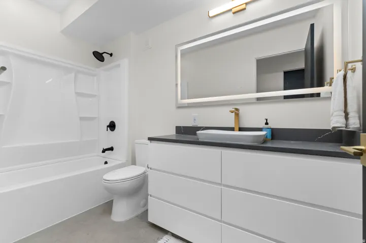 Modern bathroom featuring a single white vanity with a vessel sink, a dark countertop, and gold-finish fixtures