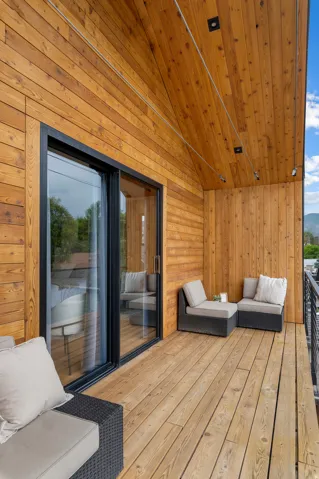 Expansive wood-planked balcony with a sloped wood-paneled ceiling, black-framed sliding glass doors, and recessed lighting