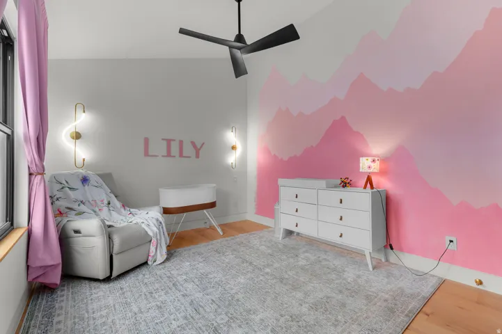 Bright room featuring wood-finish flooring, a contemporary ceiling fan, and wall-mounted sconces providing ambient lighting