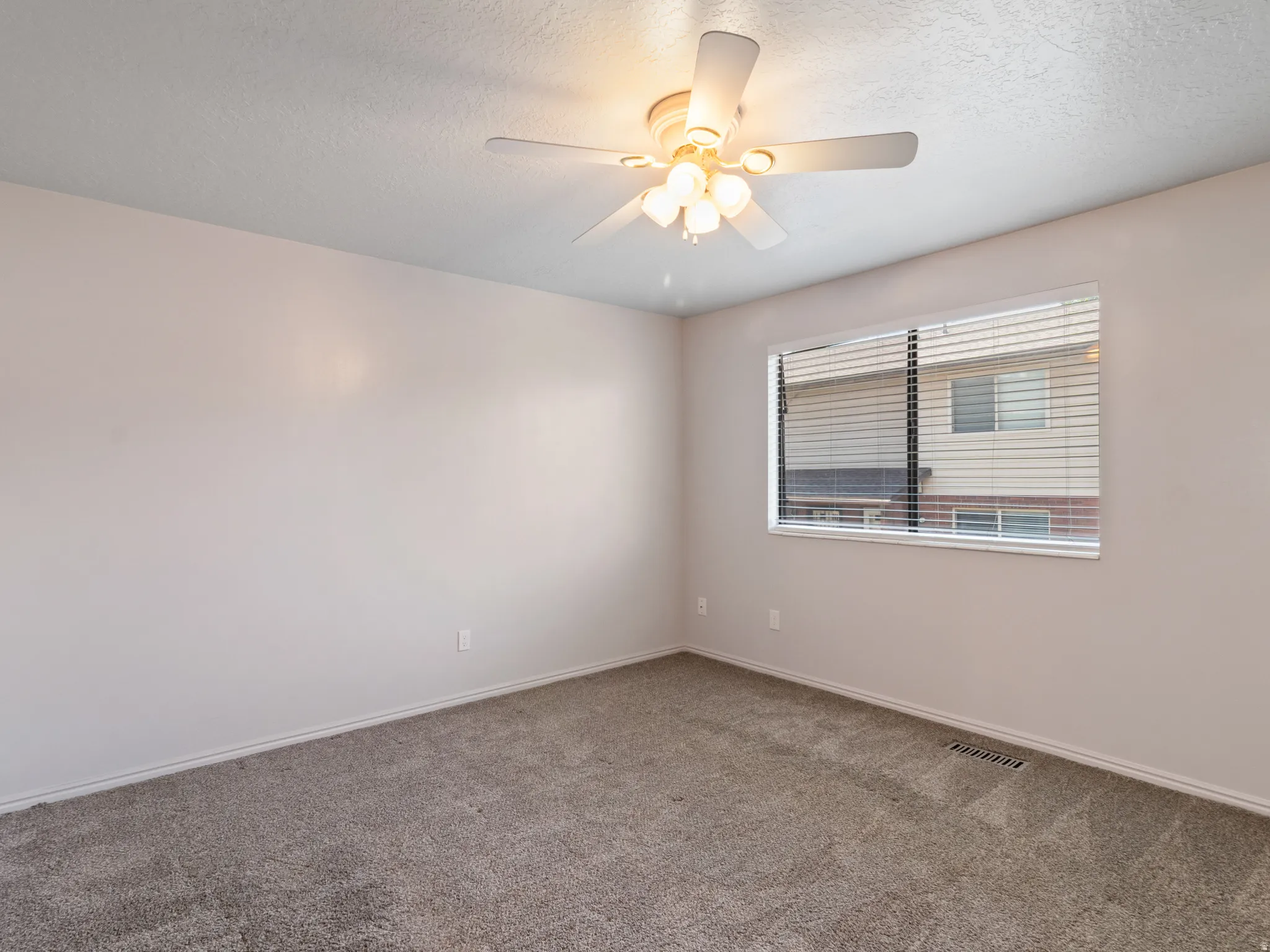 Carpeted room featuring a ceiling fan with integrated lighting, a window with horizontal blinds, and neutral wall tones