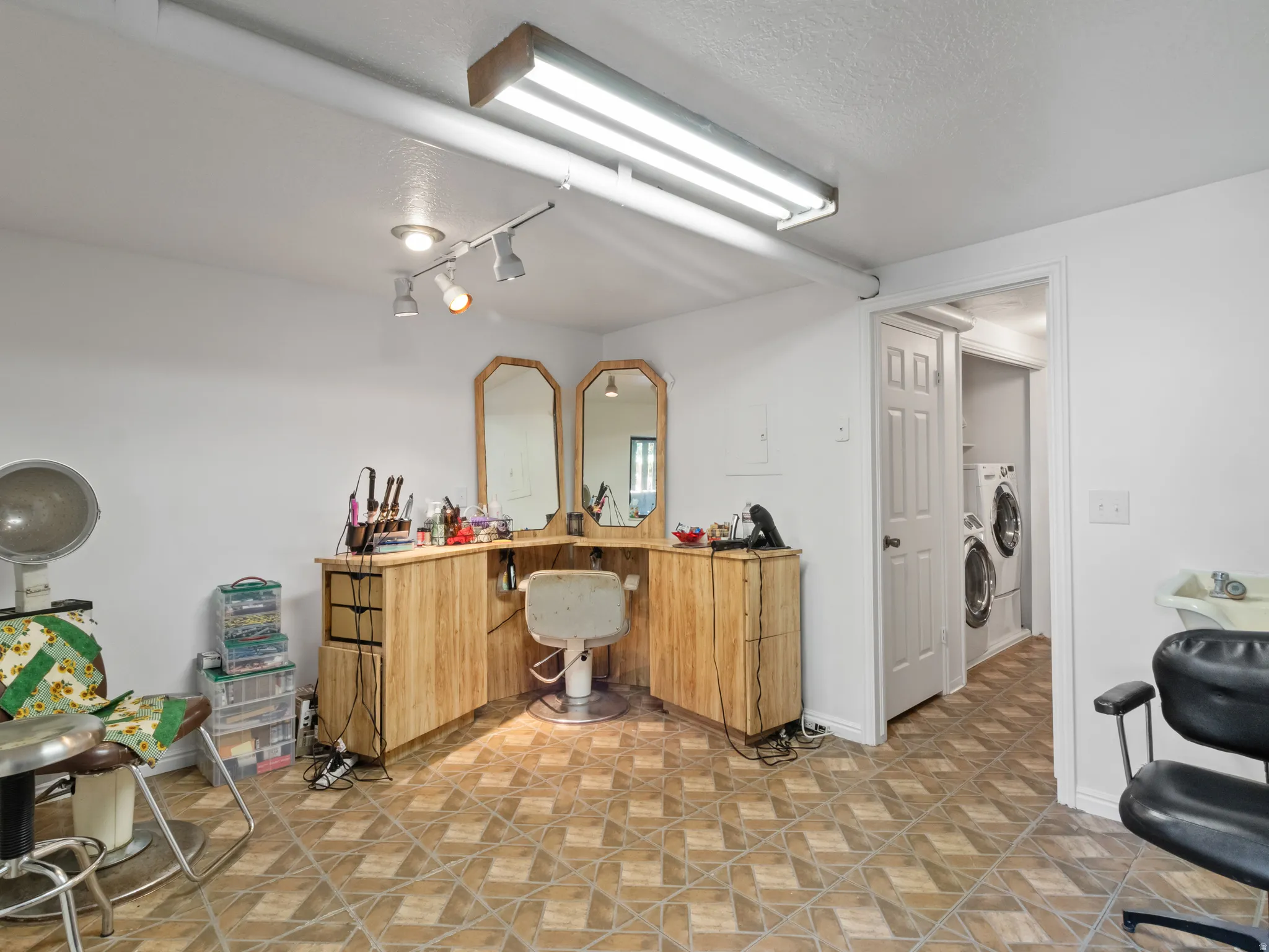 Versatile interior space featuring patterned tile flooring, a dedicated station with built-in cabinetry and mirrors, track lighting, and an adjacent utility area with a stacked washer and dryer