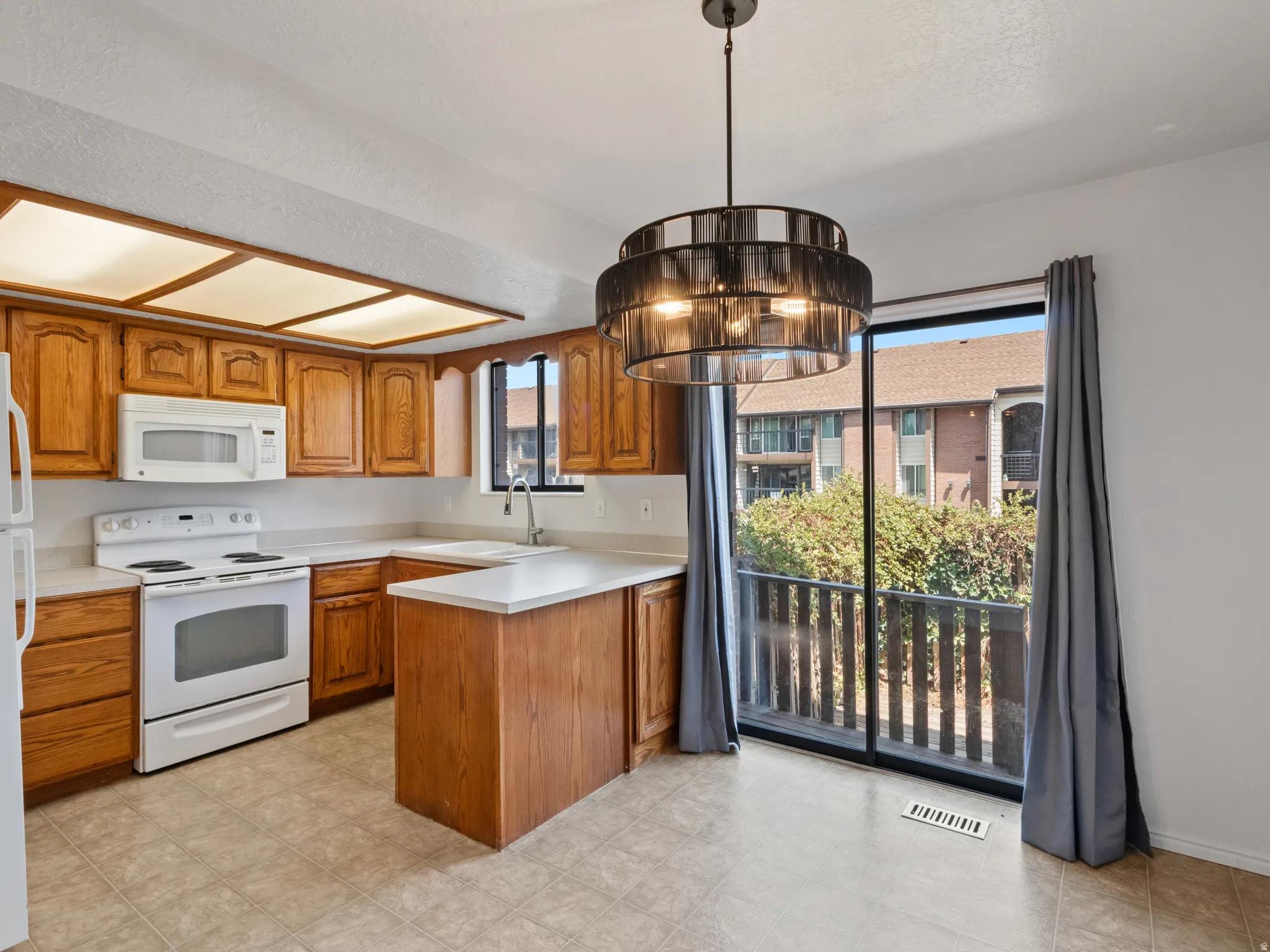 Kitchen with wood cabinetry, white appliances, and light-colored countertops