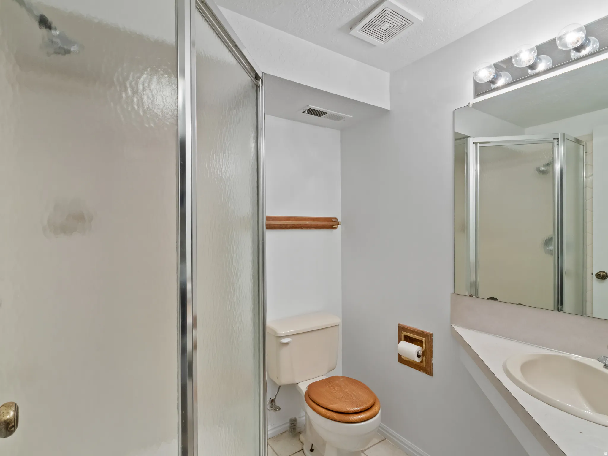 Bathroom featuring a shower stall with clear glass doors, a vanity with an integrated sink, a wall-mounted mirror, and overhead vanity lighting