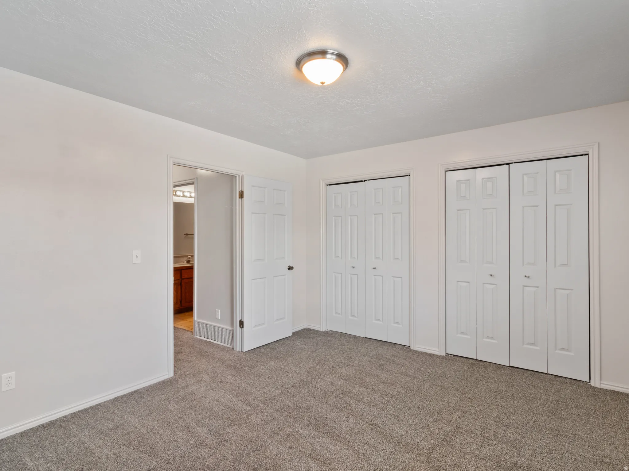 Carpeted room with white walls, featuring two sets of bi-fold closet doors and an overhead flush-mount light fixture