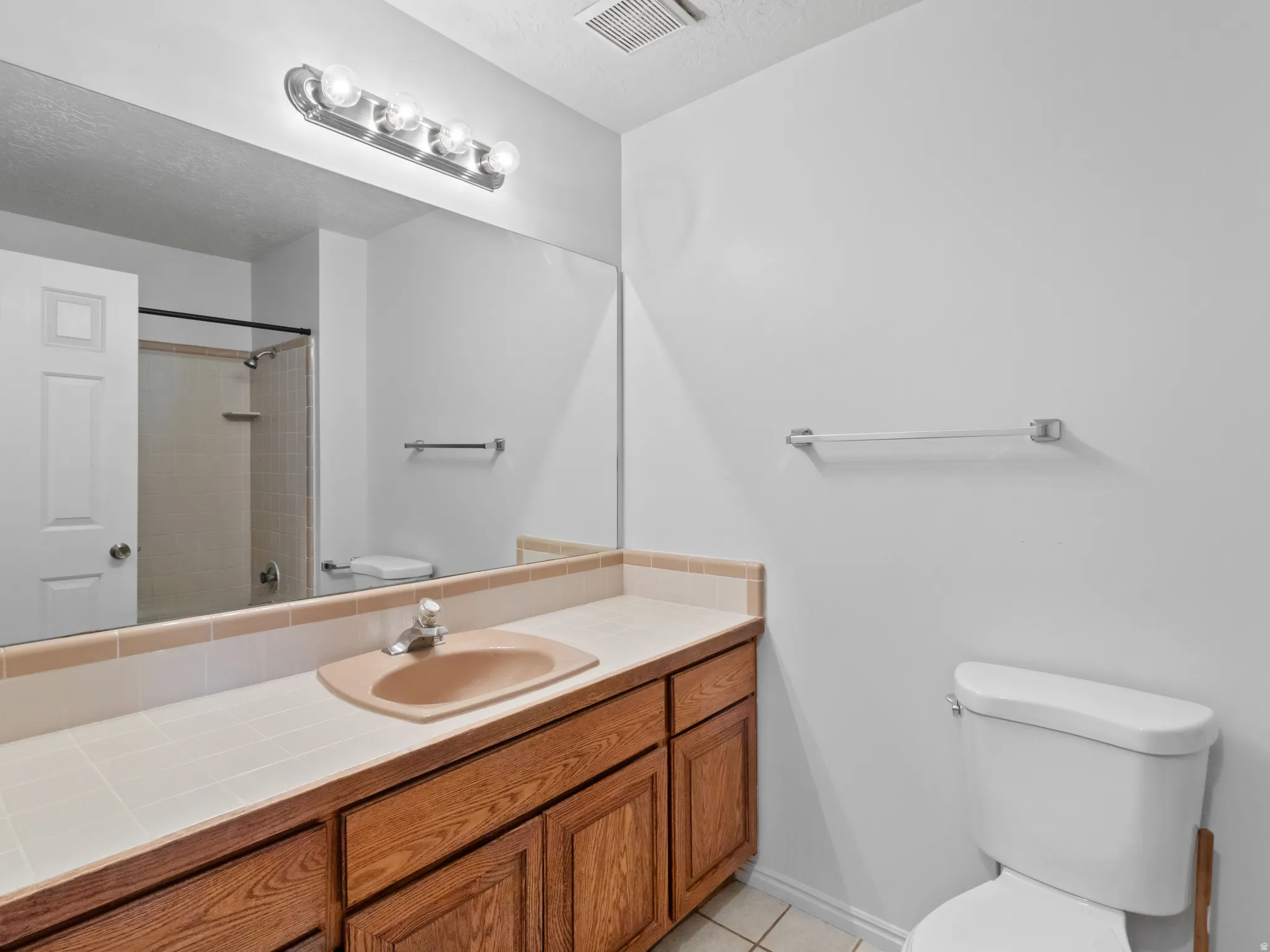 Bathroom featuring a vanity with wood-finish cabinetry, a tiled countertop, and an integrated sink basin