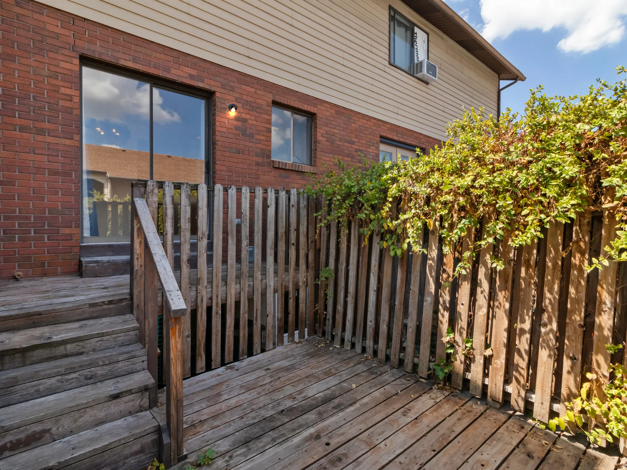 Private wooden deck area featuring a sliding glass door entry, brick exterior, and wood privacy fence with established greenery