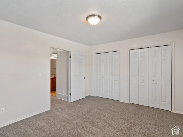 Carpeted room with white walls, featuring two sets of bi-fold closet doors and an overhead flush-mount light fixture
