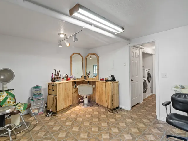 Versatile interior space featuring patterned tile flooring, a dedicated station with built-in cabinetry and mirrors, track lighting, and an adjacent utility area with a stacked washer and dryer