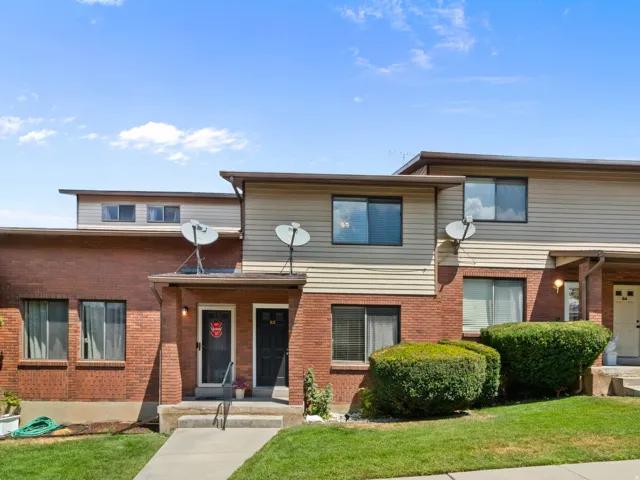 Two-story townhouse exterior featuring brick and horizontal siding, multiple windows, and a concrete walkway