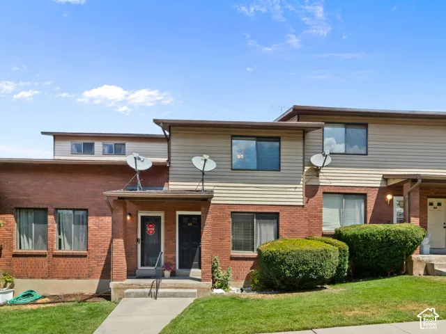 Two-story townhouse exterior featuring brick and horizontal siding, multiple windows, and a concrete walkway